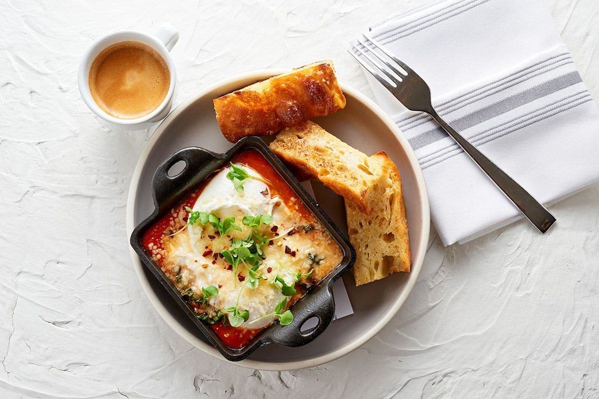 Baked eggs in tomato sauce with toasted bread and espresso